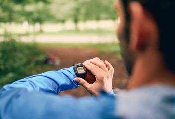 Fit male jogger day using a smartwatch during cross country forest trail race in a nature park.