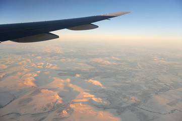 Fototapeta premium sunrise light on snow covered land under the airplane wing