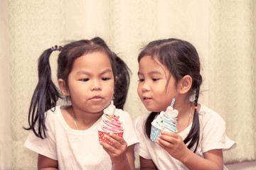 two asian little girl having fun to blowing birthday cupcake together in vintage color tone