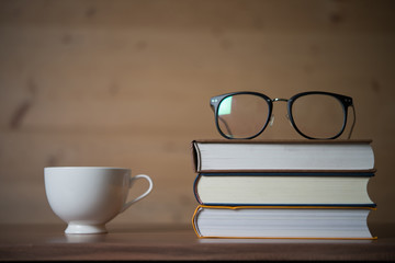 Glasses on stack of books and a cup of coffee on wooden table. Education concept.