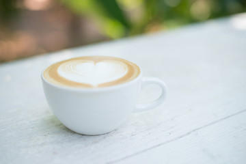 Cup of latte art heart shape coffee on white table.