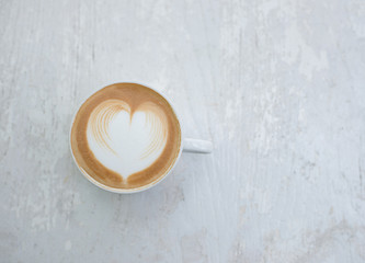 Cup of latte art heart shape coffee on white table.