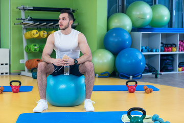 man sitting on a gym ball holding a phone after doing a work out