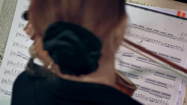 Violinist playing / Violin Player / Orchestra Musician. Female violinist plays violin at a classical music concert against Vivaldi note sheet.