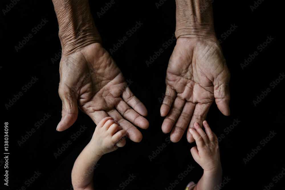 Wall mural hand of a young baby touching old hand of the elderly (soft focus and blurry)