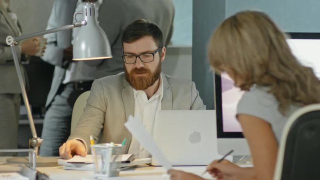 Lockdown of bearded businessman in glasses working on his laptop in busy office 
