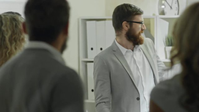 Bearded businessman in glasses giving presentation about finances before colleagues and answering questions 