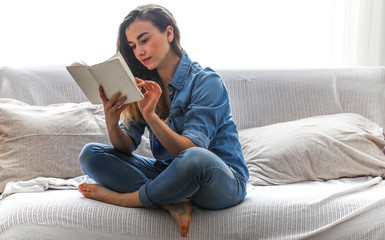 White cozy bed and a beautiful girl, reading a book, concepts of home and comfort