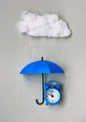 Blue alarm clock under an umbrella on gray background