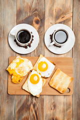 Two cups with coffee, toast and eggs on a wooden table