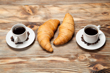 Two cups of coffee and a croissant on a wooden table