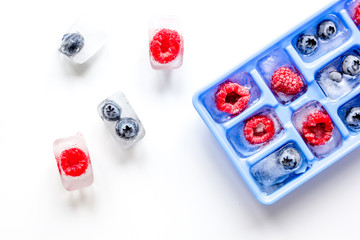 Icecubes with icetray and berries on white background top view