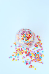 sweet confectionery sprinkling of stars shape. Colorful sugar sprinkles in glass jar on light-blue abstract background. soft focus. top view. template for design