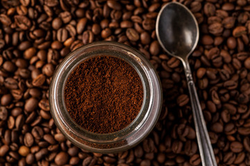 Ground coffee in a glass jar with coffee beans and metal spoon