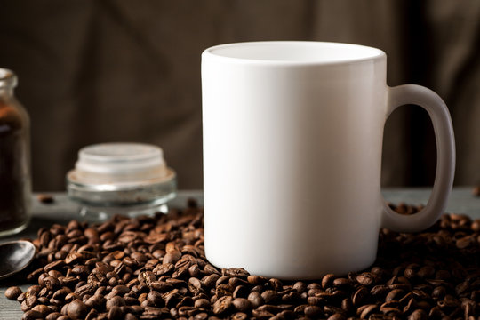 White coffee mug with coffee beans and glass jar with ground coffee inside