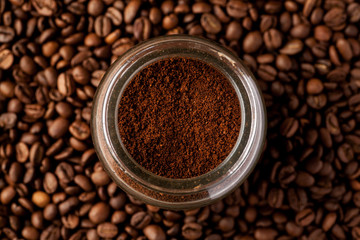 Ground coffee in glass jar among coffee beans, top view