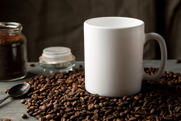White coffee mug with coffee beans and glass jar with ground coffee inside.