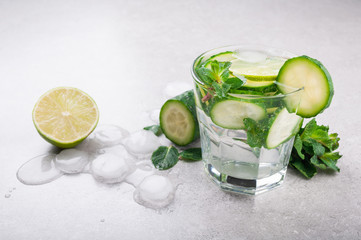 Refreshing water with cucumber, mint and ice on grey background. Summer drink cucumber lemonade. Healthy drink and detox concept