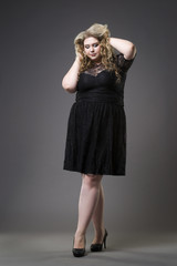 Young beautiful plus size model in black dres, xxl woman on gray studio background