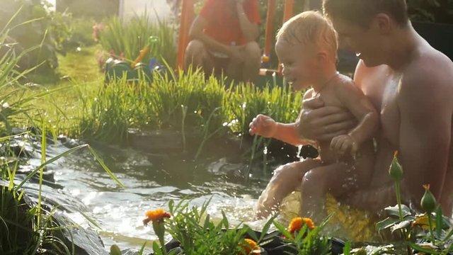 Cute little boy and his father, swimming, diving in a pool in the summer, having fun in slow motion happy grandma sitting on a swing on background beautiful flowers on foreground. 1920x1080