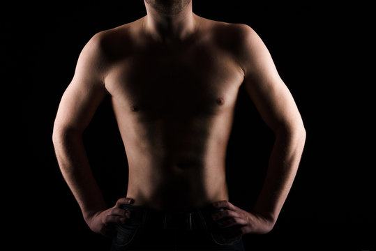 Handsome topless man without face on black background posing in studio
