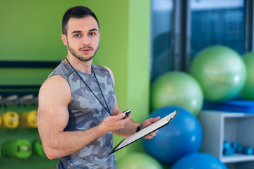 Portrait of a muscular trainer writing on clipboard