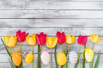 Colorful easter eggs and tulips on wooden planks.