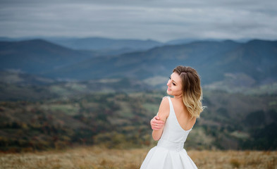 Bride holds her shoulders tender standing on the hill among the mountains