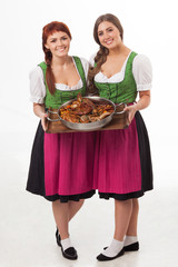 Two young caucasian women in traditional Bavarian dress are holding in the hands the dish with different type of meet food.