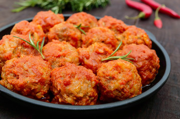 Meat balls in spicy tomato sauce served on a cast iron pan on a dark wooden background. Close up