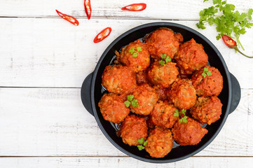Meat balls in spicy tomato sauce served on a cast iron pan on a white wooden background. The top view.