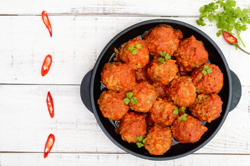 Meat balls in spicy tomato sauce served on a cast iron pan on a white wooden background. The top view.