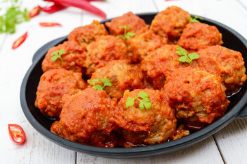 Meat balls in spicy tomato sauce served on a cast iron pan on a white wooden background. Close up