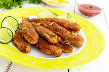 Deep frying small fish capelin on a plate on white wooden background. Close up