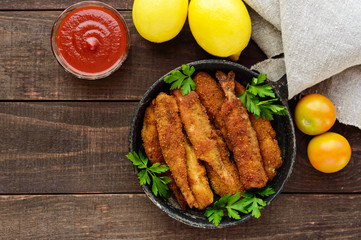 Deep frying small fish capelin in a pan on a dark wooden background. Good snack to beer.