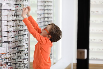 optician putting glasses to boy at optics store
