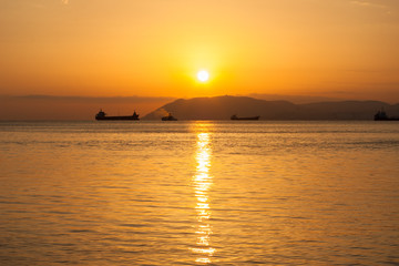Natural summer sea sunset. Silhouettes of ships and strip of land on the horizon. Orange sea sunset in evening