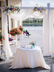 Little round table with glass box stands before beautiful wedding altar outside