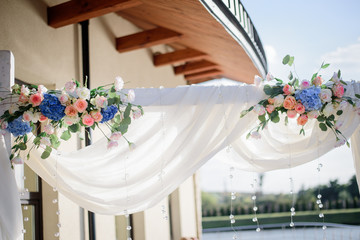Bouquets of white roses and blue hydrangeas hang on wedding altar outside