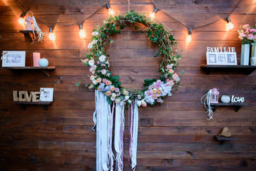 Wreath made of green leaves and flowers hangs on wooden wall