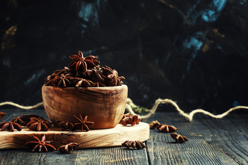 Anise stars in a wooden bowl, dark background, selective focus