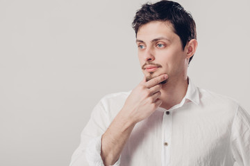 Fototapeta premium portrait of handsome young pensive man in white shirt on gray ba