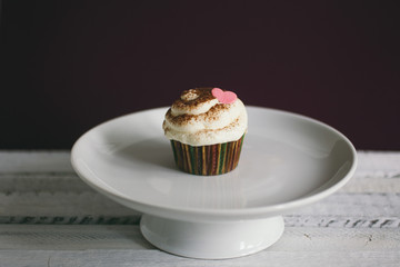 Cupcake decorated with cream, chocolate and heart shape candies on wooden table.