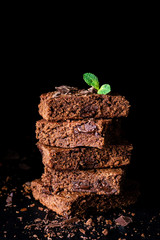 Stack of brownies with dark chocolate over black background, closeup view, vertical composition