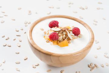 Fototapeta na wymiar Yogurt bowl with fresh raspberries, apricots and muesli in a wooden bowl on white background. Meal for healthy breakfast, diet food and healthy lifestyle
