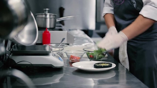 Cook puts lettuce on a white flat dish.