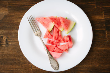 Small pieces of ripe watermelon and fork on the white plate over wooden background