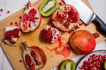 sliced fruit red pomegranate and kiwi on a cutting Board, a plate on white wooden background with knives close-up