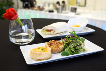 Two quiches and chicken tortilla wrap with dip on modern plates.