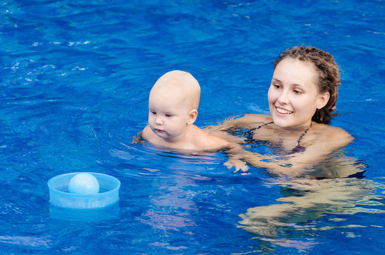 Mother and her child in the pool. Woman playing with a ball with his little daughter.